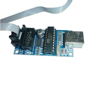 May include: A blue circuit board with various electronic components, including a USB port, integrated circuits, and a connector for a ribbon cable. The board has a silver USB port and a gray ribbon cable.