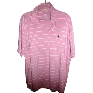May include: Pink and white striped polo shirt with short sleeves. The shirt has a collared neckline and a small pocket on the left chest. The shirt is hanging on a hanger. The brand name is visible on the collar.