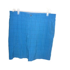 May include: Blue plaid shorts hanging on a white hanger. The shorts have a button closure and a classic plaid pattern in shades of blue and white. The shorts are made of a lightweight material.