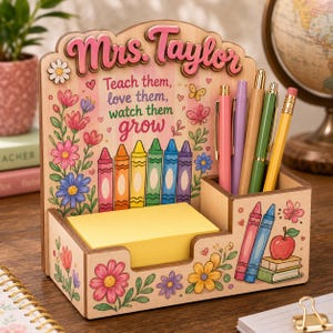 Könnte beinhalten: Ein Schreibtisch-Organizer aus Holz mit Blumenmuster, einem Stapel gelber Haftnotizen und einem Stiftehalter. Der Text lautet Mrs. Taylor und Teach them, love them, watch them grow. Er enthält Illustrationen von bunten Wachsmalstiften, Blumen, Schmetterlingen und einem Apfel.