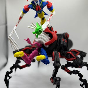 Pode incluir: Escultura colorida impressa em 3D, apresentando uma figura de bobo da corte com rosto de caveira sobre uma estrutura mecânica semelhante a uma aranha. O bobo da corte usa uma roupa azul, amarela e vermelha. A aranha é preta com detalhes vermelhos.