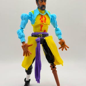 Peut inclure: Une figurine de pirate portant un tricorne noir, une chemise à col bleu clair, un gilet jaune avec des marques rouges et une écharpe violette. La figurine a un pantalon noir, une chaussure noire et une jambe de bois marron. Articulée.