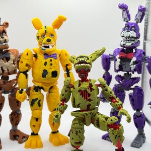 May include: Four articulated action figures featuring weathered, robotic designs. From left to right: a brown bear with a top hat, a yellow rabbit with a purple bowtie, a green rabbit with an exposed red interior, and a purple rabbit with a red bowtie.