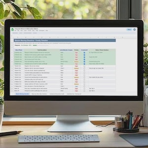 May include: A computer monitor displaying a digital moving checklist spreadsheet titled House Moving Checklist - Family Timeline, featuring columns for task descriptions, assigned members, status, and checkboxes on a desk.