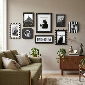 May include: A gallery wall arrangement featuring eight black and white picture frames in various shapes and textures, including rectangular, square, and scalloped edges, displaying monochrome photographs of people, architecture, and pets.