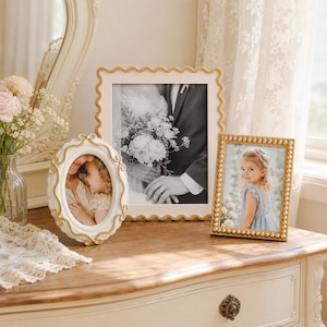 Puede incluir: Tres marcos de fotos decorativos expuestos juntos. Uno es un marco ovalado blanco con volutas doradas, otro es un marco cuadrado grande con borde festoneado y otro es un marco rectangular con un borde dorado de cuentas, cada uno con una foto.