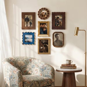 May include: A gallery wall arrangement featuring six diverse picture frames in various shapes and finishes, including wood, gold, and blue, displaying photographs of people, a dog, and a still life, mounted on a wall above a floral patterned armchair.