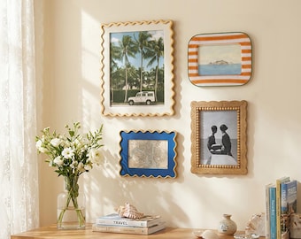 May include: Four wall-mounted picture frames with distinct designs: a large cream wavy frame, a small orange and white striped frame, a medium blue wavy frame, and a medium wooden beaded frame, all displaying various photographs and prints.