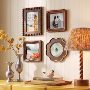Peut inclure: Quatre cadres muraux en bois de formes variées, dont un cadre rectangulaire perlé, un cadre carré, un cadre carré ondulé et un cadre en forme de fleur, affichant chacun une photographie différente, disposés sur un mur au-dessus d'une surface.