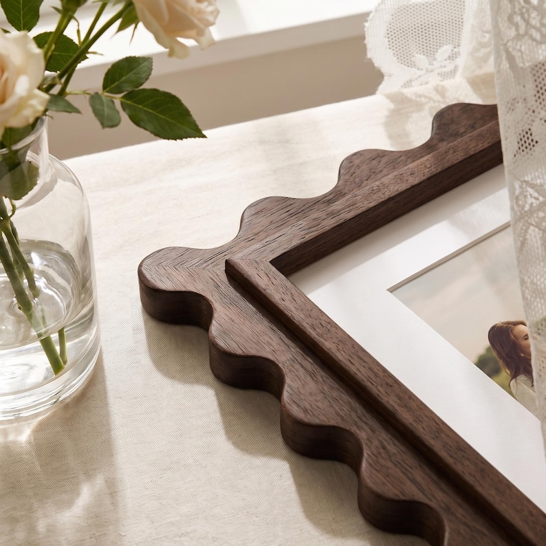 May include: A rectangular picture frame crafted from dark brown wood with a distinct scalloped, wavy edge design. The frame features a white mat board surrounding a photograph, showcasing a visible wood grain texture throughout the frame.