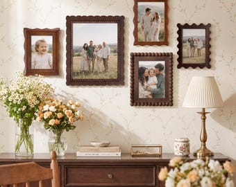 May include: A gallery wall arrangement featuring five dark wood picture frames with scalloped or beaded edges, displaying family photographs. The frames are mounted on a wall with floral wallpaper above a wooden sideboard with decor items.