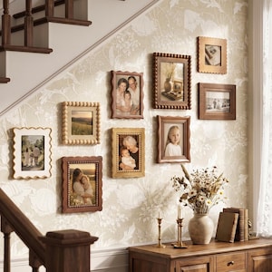 Könnte beinhalten: Eine Galeriewand mit neun rechteckigen Bilderrahmen in verschiedenen Holztönen und Texturen, darunter perlenartige und gewellte Ränder. Die Rahmen zeigen verschiedene Fotografien und sind an einer Wand mit hellem Blumenmuster angebracht.