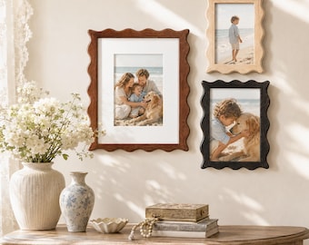 May include: Three scalloped-edge picture frames in dark brown, light wood, and black finishes are mounted on a wall. Each frame contains a photograph of people and a dog on a beach. The frames are displayed above a wooden console table.