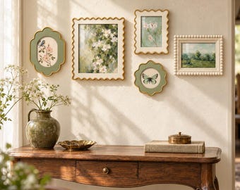 May include: A collection of five wall-mounted picture frames featuring scalloped and beaded edges in gold and cream tones, displaying botanical and landscape art, arranged above a wooden console table with a ceramic vase and small box.