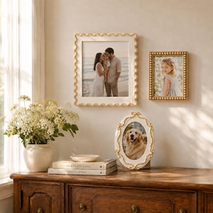 Può includere: Una collezione di tre cornici: una grande cornice rettangolare con bordo dorato ondulato, una cornice rettangolare più piccola con bordo dorato a perline e una cornice ovale con decorazioni dorate. Ogni cornice contiene una fotografia.