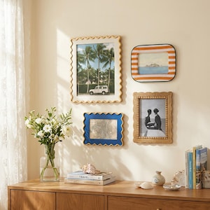 May include: A collection of four wall-mounted picture frames featuring diverse designs: a large cream scalloped frame, a horizontal orange and white striped frame, a small blue scalloped frame, and a vertical wooden frame with beaded detailing.
