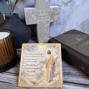 May include: A religious-themed display featuring a wooden cross with the text "FOR THIS child I HAVE prayed" and a framed image of Jesus with the text "But take heart! I have overcome the world." A closed Holy Bible is also present.