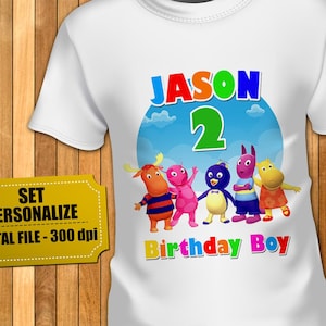 Peut inclure: Un t-shirt blanc avec un graphique représentant cinq personnages de dessin animé Backyardigans. Au-dessus des personnages se trouvent le nom JASON en bleu et le chiffre 2 en vert. Sous les personnages, le texte Birthday Boy en lettres multicolores.