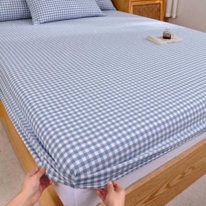 Könnte beinhalten: Ein Spannbettlaken mit blau-weißem Vichy-Muster ist über einen Holzrahmen gespannt. Das Laken bedeckt Matratze und Kissen und sorgt für ein stimmiges Aussehen. Die Bettwäsche ist hellblau.