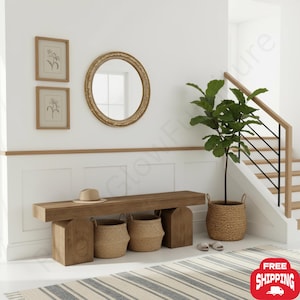 May include: A wooden bench with two arched supports, featuring a beige hat on top and two woven baskets underneath. Beside the bench stands a tall green plant in a woven pot, with a round gold-framed mirror and two framed botanical prints above.