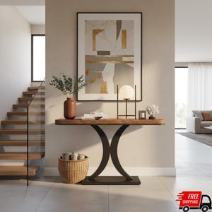 May include: A modern entryway scene featuring a wooden console table with a black metal base. The table is adorned with a lamp, vase, books, and decorative items. A large abstract art piece hangs above the table, and a woven basket sits below.