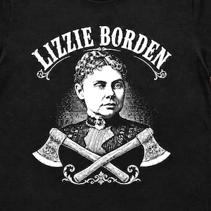 May include: A black short-sleeved t-shirt featuring a white graphic print of a portrait of Lizzie Borden with the text "LIZZIE BORDEN" arched above her head and two crossed axes positioned below her chest in a detailed, vintage-style illustration.