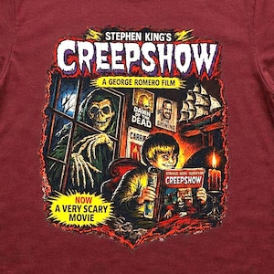 May include: A maroon short-sleeve t-shirt featuring a graphic print of the movie poster for Stephen King's Creepshow. The design includes a skeleton, a child, and text that reads Stephen King's Creepshow, A George Romero Film, and Now A Very Scary Movie.