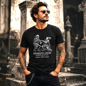 May include: A black short-sleeved t-shirt featuring a white graphic print of a skeleton and a figure. The text reads MEMENTO MORI, REMEMBER YOU MUST DIE, HOLBEIN, and DANSE MACABRE. The shirt has a crew neckline and a standard fit design.