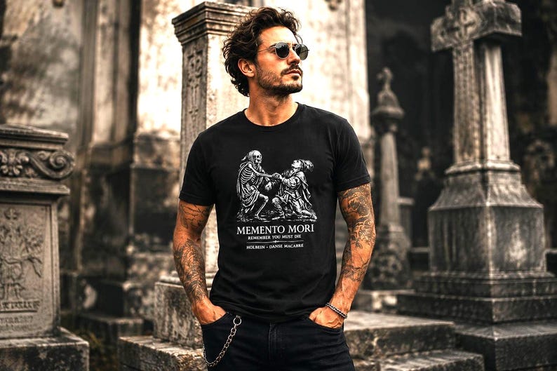May include: A black short-sleeved t-shirt featuring a white graphic print of a skeleton and a figure. The text reads MEMENTO MORI, REMEMBER YOU MUST DIE, HOLBEIN, and DANSE MACABRE. The shirt has a crew neckline and a standard fit design.