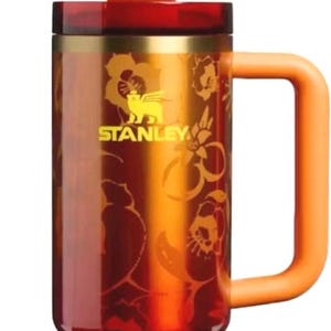 K&ouml;nnte beinhalten: Ein Stanley-Reisebecher mit goldenem Ananas-Aufsatz und Griff. Der Becher ist rot und orange mit einem floralen Design und dem Stanley-Logo. Der Griff und der Strohhalm sind orange.