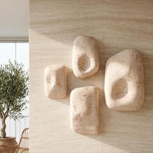 May include: A set of four beige, organic-shaped wall sculptures with recessed centers mounted on a light-colored, textured stone wall. The sculptures feature a porous, natural finish and are arranged in a cluster on the vertical surface.