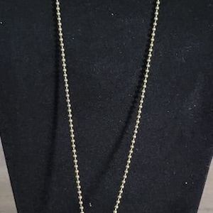 May include: A gold chain necklace with a cross pendant featuring a bullet casing in the center. The cross has intricate details and is displayed on a black velvet cushion.