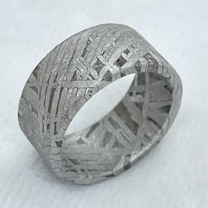 May include: A wide band ring crafted from metallic material featuring a distinct, etched cross-hatch pattern across its entire outer surface. The ring has a matte, silver-grey finish with visible intersecting lines that create a textured, geometric appearance.
