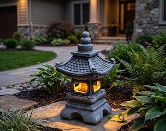 May include: A gray stone-textured garden lantern with a tiered roof and a spherical finial. The central chamber features a warm, glowing yellow light visible through rectangular openings on the sides, resting on a flat stone surface in a garden.