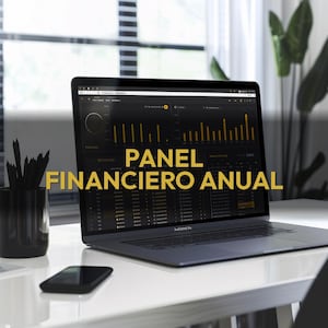 May include: A laptop displaying a financial dashboard with the text "PANEL FINANCIERO ANUAL" in gold. The laptop is on a white desk with a black smartphone and a black pencil holder. A window and a plant are in the background.