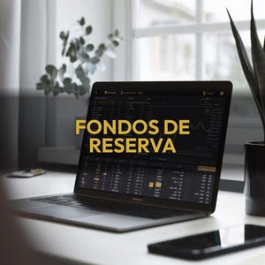 May include: A laptop displaying financial data with the text "FONDOS DE RESERVA" in gold. The laptop is open on a white desk, with a smartphone and a plant in the background. The screen shows charts and numbers.