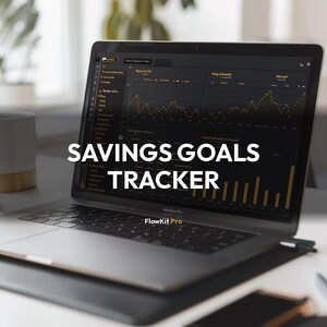 May include: A laptop displaying a financial graph with the text "SAVINGS GOALS TRACKER." The screen shows a dark interface with yellow data lines and bar graphs. The laptop is open on a white desk, with a phone and a mug nearby.