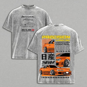 May include: Gray t-shirt featuring a front graphic with "NISSAN Fairlady" and "Datsun 240Z" text, plus a "Nismo" logo. The back displays an orange car graphic with "PRECISION HANDLING UNMATCHED CONTROL" and "SILVIA S15" text.