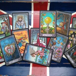May include: A spread of tarot cards on a red, white, and blue patterned surface. The cards feature dark gray borders with intricate designs and colorful illustrations. The cards include "Page of Pentacles", "Five of Wands", "Ace of Pentacles", "Ten of Cups", "Temperance", "The Devil", "The Fool", and "Three of Swords".