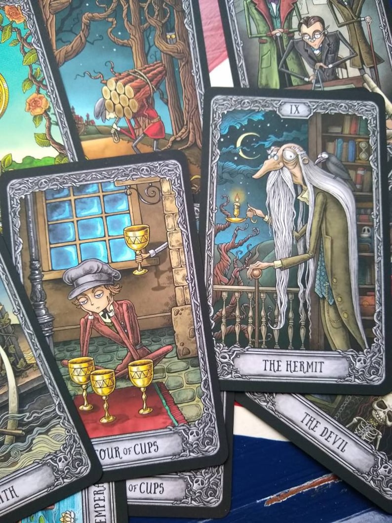 May include: A set of tarot cards with black borders and silver accents. The cards feature illustrations of people and scenes in a dark, gothic style. The cards include "The Hermit", "The Devil", and "Four of Cups".