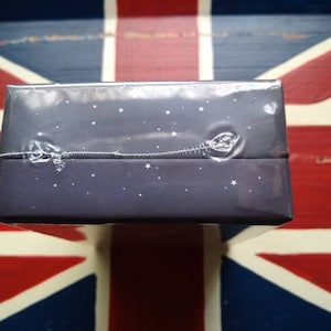 May include: A dark blue box with a starry night design. The box is wrapped in clear plastic.