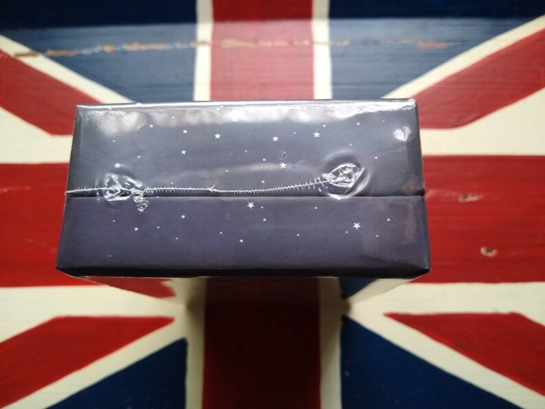 May include: A dark blue box with a starry night design. The box is wrapped in clear plastic.