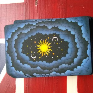May include: A deck of cards with a dark blue background and a yellow sun, white moon, and stars in the center. The cards are stacked on a red, white, and blue surface.