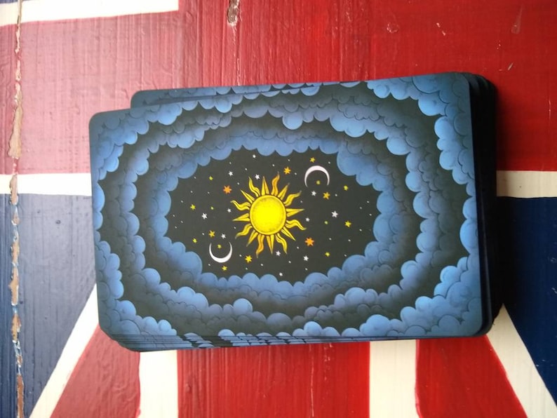 May include: A deck of cards with a dark blue background and a yellow sun, white moon, and stars in the center. The cards are stacked on a red, white, and blue surface.
