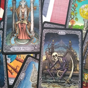 May include: Tarot cards with black frames and ornate silver designs. The cards depict the High Priestess, Death, and Temperance. The High Priestess card shows a woman in a long robe sitting on a throne. The Death card shows a skeletal figure sitting on a throne with a scythe. The Temperance card shows a winged figure pouring water from one cup to another.