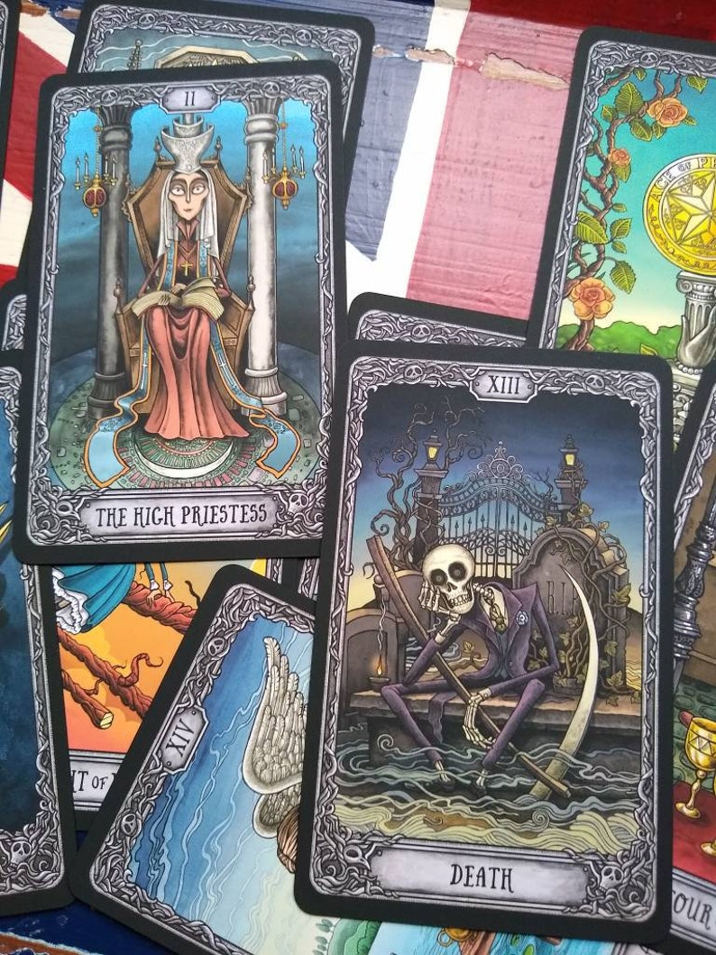 May include: Tarot cards with black frames and ornate silver designs. The cards depict the High Priestess, Death, and Temperance. The High Priestess card shows a woman in a long robe sitting on a throne. The Death card shows a skeletal figure sitting on a throne with a scythe. The Temperance card shows a winged figure pouring water from one cup to another.