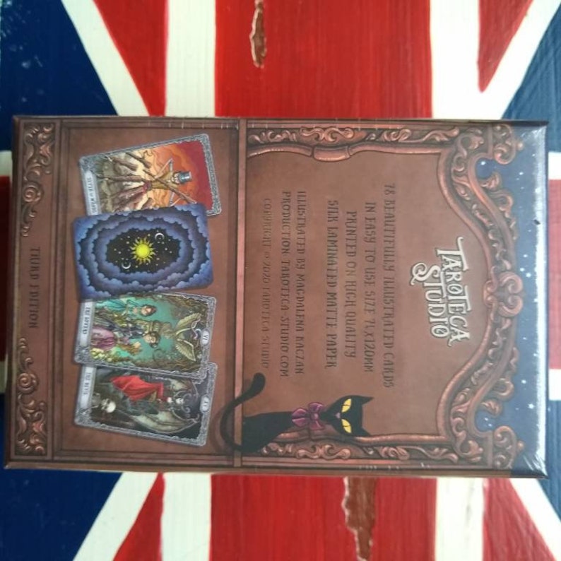 May include: A box of Tarot cards with a black cat illustration on the back. The box is decorated with a gold frame and features the text "Tarotca Studio" and "78 beautifully illustrated cards".