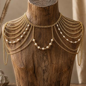 May include: A gold-toned body chain necklace featuring multiple draped chain layers that extend over the shoulders. The design incorporates small, white, oval-shaped pearls interspersed along the chains, creating a cascading effect across the chest.