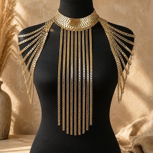 Puede incluir: Un collar de cuerpo de metal dorado con una gargantilla ancha y estructurada compuesta por pequeños eslabones rectangulares. Múltiples cadenas verticales largas cuelgan del cuello sobre el pecho, con cadenas adicionales sobre los hombros.