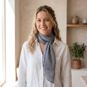 May include: A woman wearing a white button-down shirt and a navy and white gingham scarf. The scarf is draped around the neck. The woman is smiling, with blonde hair and gold hoop earrings.